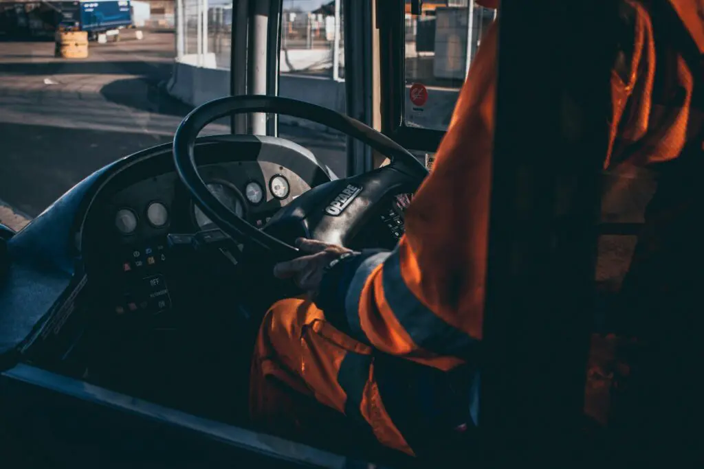 Bus driver operating vehicle from the cockpit in an industrial setting, showcasing control and focus.